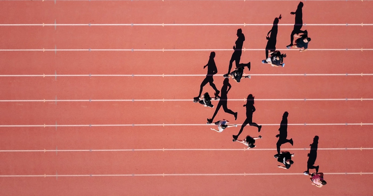 Overhead view of runners striding across the red lanes of a running track.